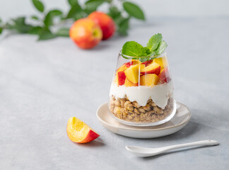 Yogurt parfait with peach and granola in a glass on a light background with fresh fruits. Healthy eating concept.