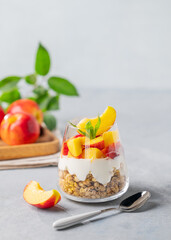 Yogurt parfait with peach and granola in a glass on a light background with fresh fruits. Healthy eating concept.