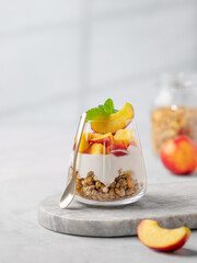 Greek yogurt parfait with peach and muesli in a glass on a marble board on a light background with...