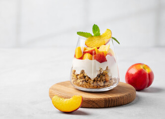Yogurt parfait with peach and granola in a glass on a wooden board on a light background with fresh...