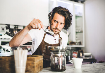 Handsome barista working in coffee shop, preparing coffee. University student working part-time in...