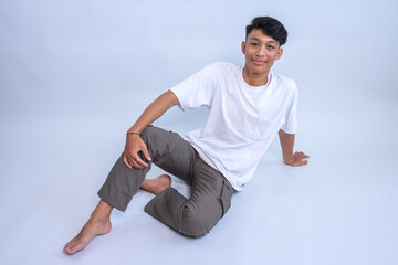 Young Asian man wear white t-shirt sitting on the floor against grey background