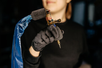 Close up tattoo master hand in black gloves holding a tattoo machine on black background.