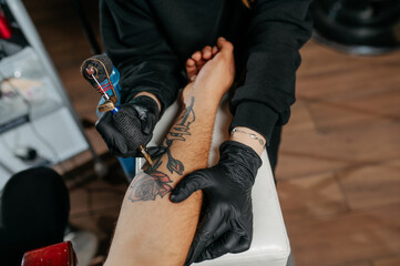 Close up tattoo master  professional tattoo artist in black gloves making a  rose tattoo on a man's...
