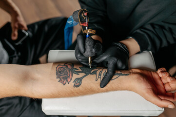 Close up tattoo master  professional tattoo artist in black gloves making a  rose tattoo on a man's...
