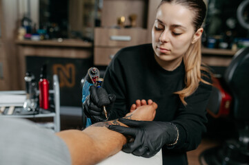 Young woman professional tattoo artist in black gloves making a rose tattoo on a man's forearm.