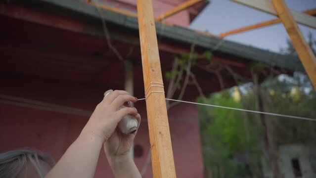a woman ties ropes around a frame for a grape bush.