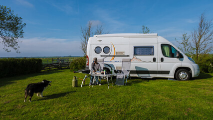A brown dog sits contentedly on the grass beside a vibrant RV against a backdrop of Texel,...
