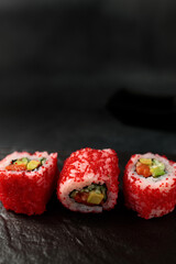 Japanese food: sushi, California roll with salmon, avocado, tobiko caviar, cucumber. Black background