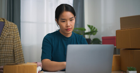 Portrait of  Young asian woman business owner sitting at desk use laptop while check orders and...