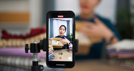 Selective focus, Young asian woman business owner selling clothes live streaming on mobile phone and packed clothes into box for a customer ,Online Shopping