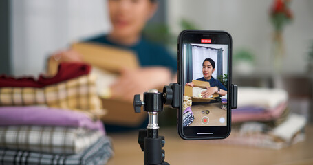 Selective focus, Young asian woman business owner selling clothes live streaming on mobile phone and packed clothes into box for a customer ,Online Shopping