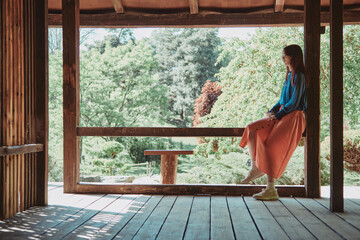 Teenage girl enjoying a peaceful moment alone in a wooden gazebo, surrounded by lush greenery....