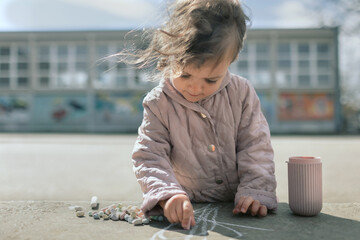 Young girl drawing with crayons on street. Creative toddler kid playing with crayons outside.