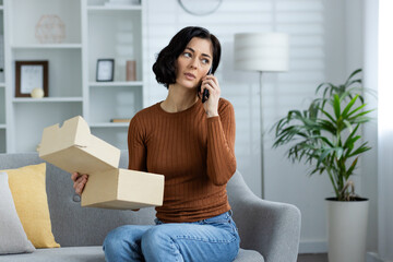 Woman talking on phone holding open box while sitting on sofa at home