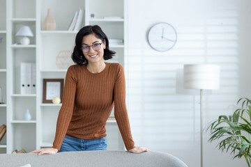 Smiling woman at home office in casual wear standing by a couch