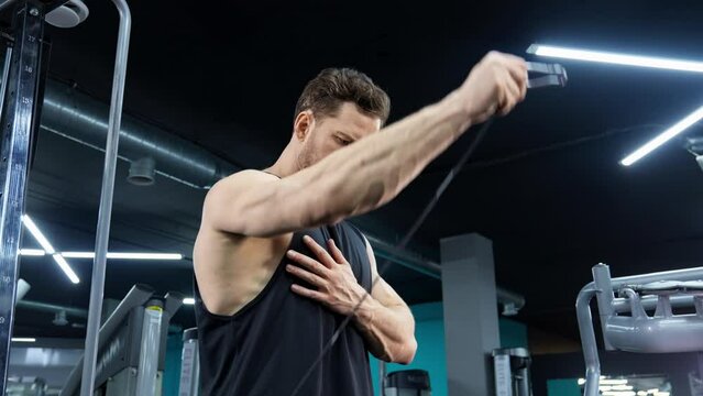 Athletic man in modern gym training with crossover machine. Shoulder training. Young athlete doing shoulders workout. Man is focused and determined. Building muscles indoors. Athlete in tank top. 4K