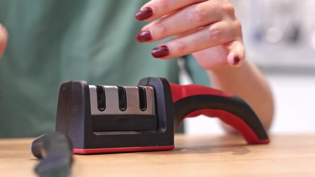 Close-up of woman sharpening knife with special knife sharpener at home	