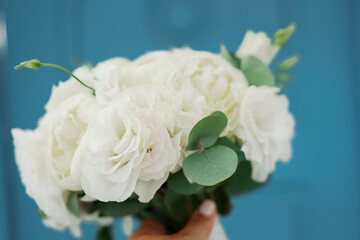 A bouquet of white flowers is being held by a person. The flowers are arranged in a vase and are placed on a blue background. The bouquet has a simple and elegant design.