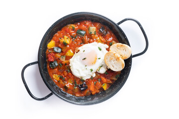 Vegetable pisto manchego with tomatoes, zucchini, peppers, onions,eggplant and egg, served in frying pan isolated on white background
