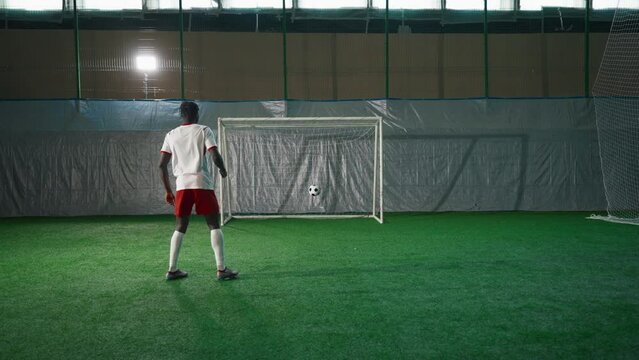 Black soccer player exercising penalty in training hall, scoring goal, back view