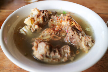 Sop Iga sapi is Beef Rib Soup is a clear soup of broth with beef ribs as the main ingredient. Served with leeks, sprinkled by sliced scallions and fried shallots. Street food, wooden table.