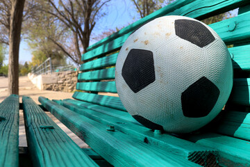 A soccer ball on a wooden bench in a park left by a child