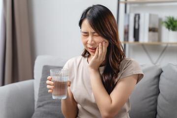 The woman with a toothache is holding her cheek in pain and a glass of water.