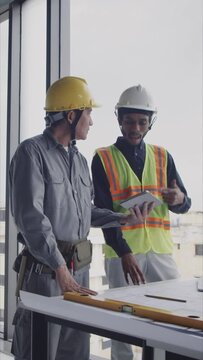 Vertical shot of diverse construction workers using digital tablet while examining workplan