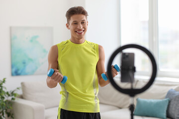 Smiling sports blogger working out with dumbbells while streaming online fitness lesson at home