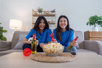 Lesbian couple cheering for Euro football with drinks and popcorn at home. Concept of sports enthusiasm and LGBTQ pride