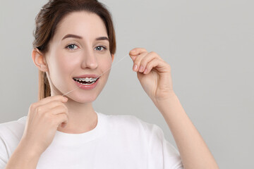 Smiling woman with braces cleaning teeth using dental floss on grey background