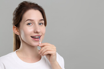 Smiling woman with dental braces cleaning teeth using interdental brush on grey background. Space for text