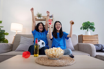 Lesbian couple cheering for Euro football with drinks and popcorn at home. Concept of sports enthusiasm and LGBTQ pride