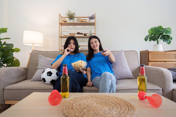 Lesbian couple cheering for Euro football at home with popcorn and drinks. Concept of sports enthusiasm and LGBTQ pride