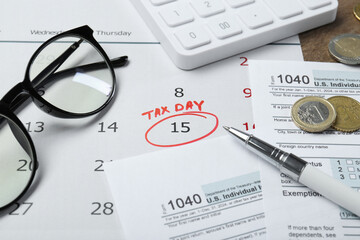 Calendar with date reminder about tax day, documents, pen, coins, glasses and calculator on table, closeup