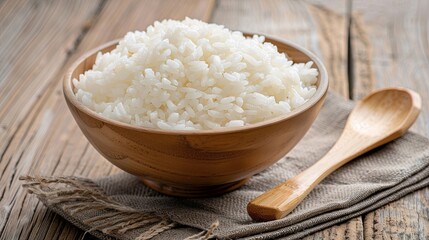 A wooden bowl filled with cooked white rice sits on a wooden table next to a wooden spoon. Generative AI