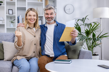 Obraz premium Joyful couple receiving great news in their living room, expressing excitement and happiness. Celebration concept with a cheerful atmosphere