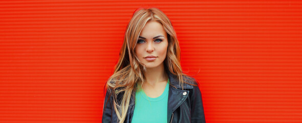 Portrait beautiful young blonde woman posing in black leather jacket on colorful orange background