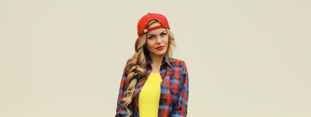 Portrait of stylish young blonde woman in red baseball cap posing on white wall background