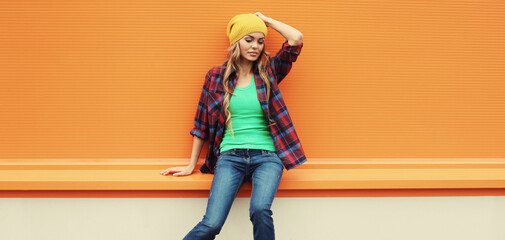 Beautiful young blonde woman posing in yellow hat, casual shirt on colorful orange background