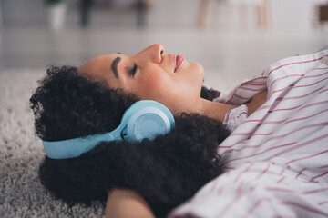 Photo of positive dreamy woman dressed striped shirt headphones enjoying music arms behind head...
