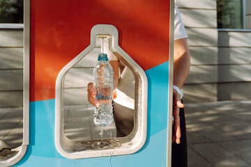 A woman pours drinking water into a water bottle in the city at a gas station. Sustainable...