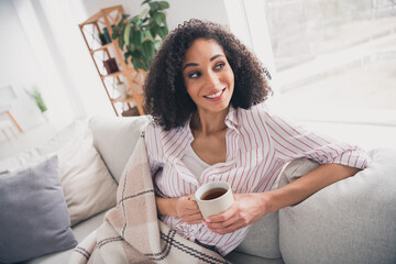 Photo of shiny dreamy girl dressed white striped shirt smiling enjoying hot cacao indoors house...