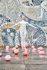 Young hairless girl ballerina with alopecia in white futuristic suit dancing outdoor and jumps...