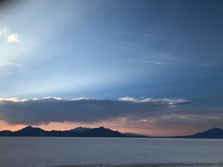 Fototapeta premium the sun sets behind the mountains in a remote area near an ocean