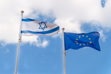 The Israeli flag and the EU flag fly against the sky. Cooperation and mutual support between Israel...