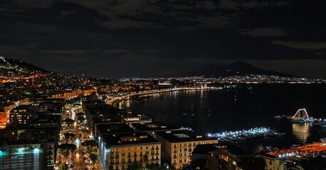 Aerial view of a cityscape near the shore, glowing with vibrant lights in the night