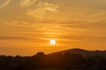 Scenic landscape featuring a hill with trees and mountains, illuminated by a glowing sunrise
