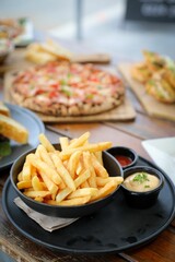 several plates of french fries on table next to pizzas